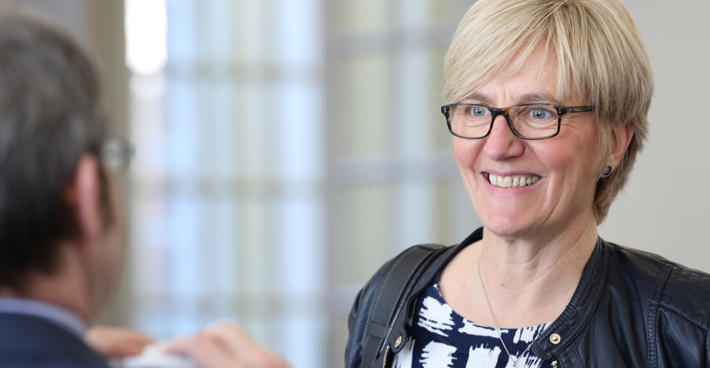 A woman facing a man whose back is to camera and blurred. She seems to be smiling at something he is saying.