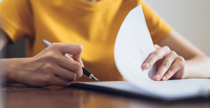 Detail of a woman in a bright yellow top writing in a document with a nice pen