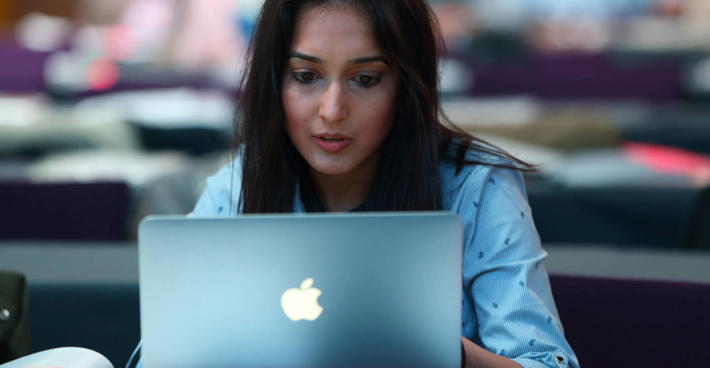 A woman sits over an open laptop, concentrating.