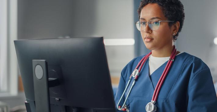 Junior doctor standing at computer in scrubs